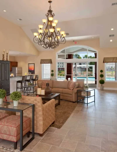 A spacious community clubhouse interior featuring high vaulted ceilings, a large ornate chandelier, a comfortable seating area