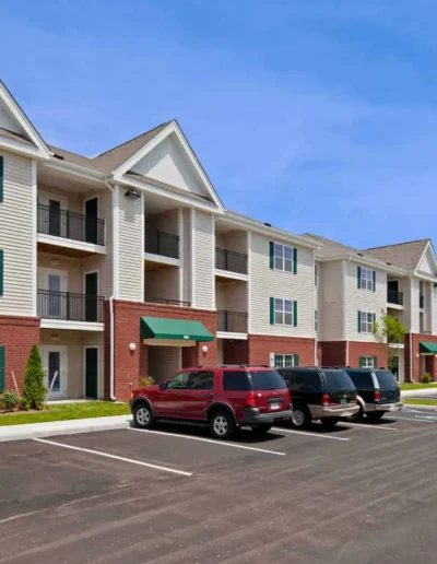 The exterior of a multi-story residential apartment building featuring beige siding, red brick accents